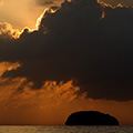 indonésie: Vycházející slunce kreslí úžasné obrazce po obloze, jak svítí zpoza mraků.